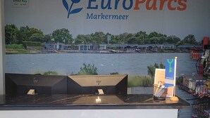 A reception area with a large EuroParcs Markermeer sign, a view of a water body, and a counter with a green key sign. - Europarcs Markermeer (Bovenkarspel)