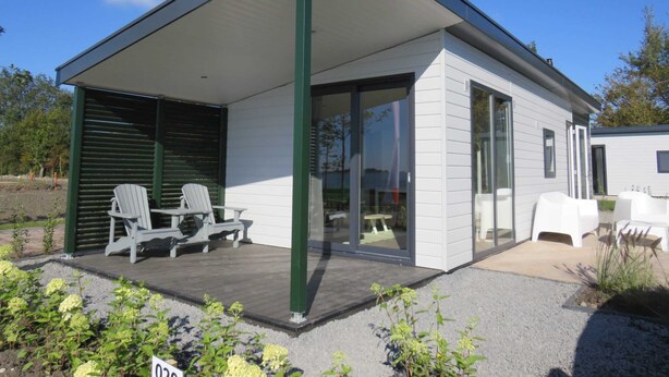 A modern single-story house with a covered patio, a dining area with a table and chairs, and a small garden area with plants. - Europarcs Markermeer (Bovenkarspel)