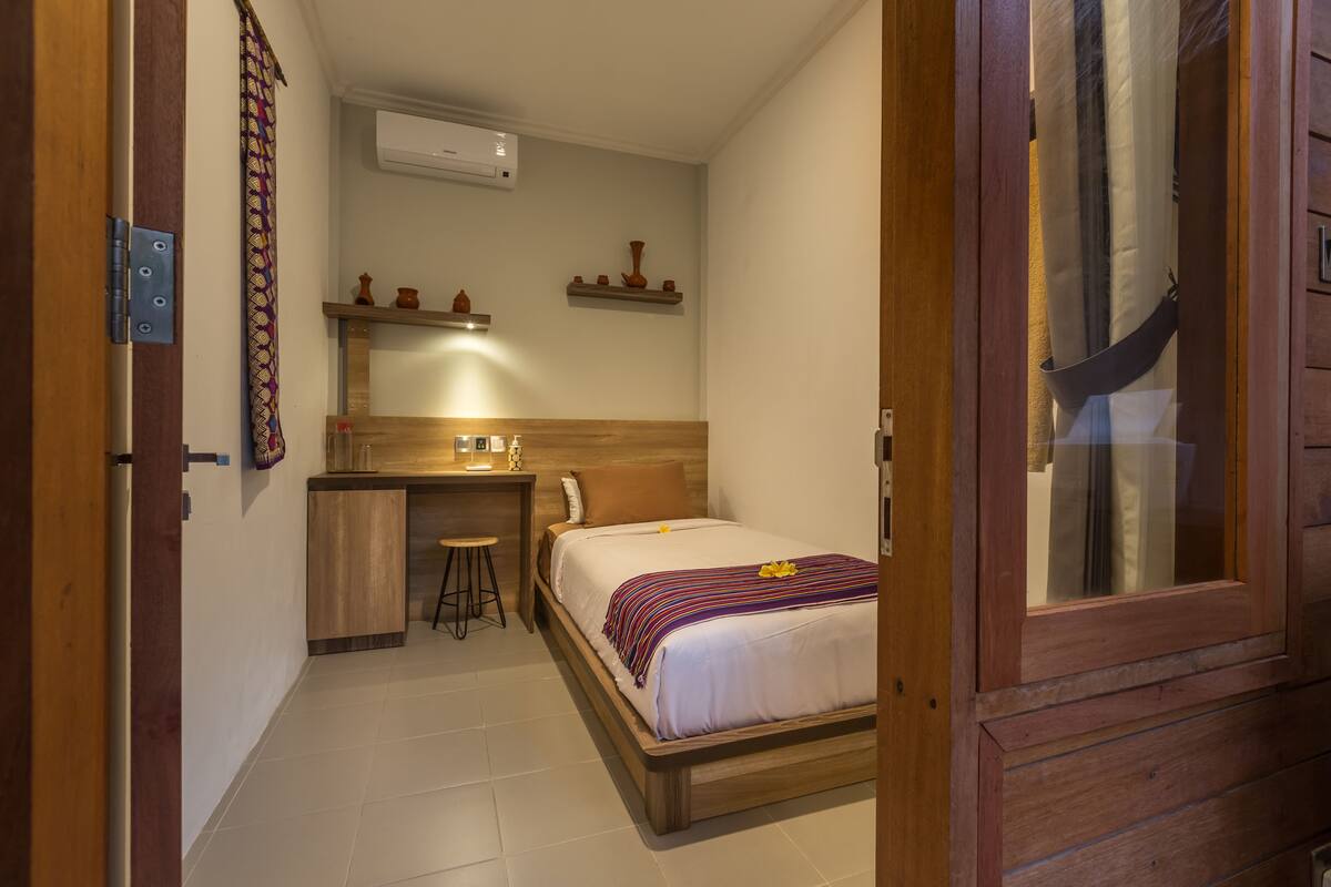 A compact hotel room with a bed, a small desk, and a shower area.