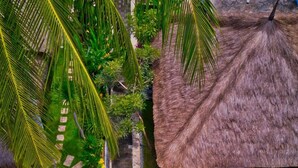 A thatched-roof structure with a stone pathway leading to it, surrounded by lush greenery and a palm tree. - Village Vibes Lombok (Kuta)