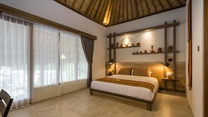 A bedroom with a large bed, a wooden headboard, a ceiling with a patterned design, and a shelf with decorative items. - Village Vibes Lombok (Kuta)