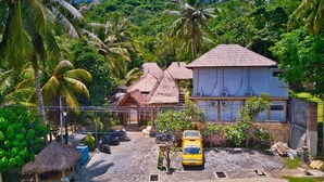 A tropical setting with a thatched-roof house, a modern building, and a yellow taxi. - Village Vibes Lombok (Kuta)