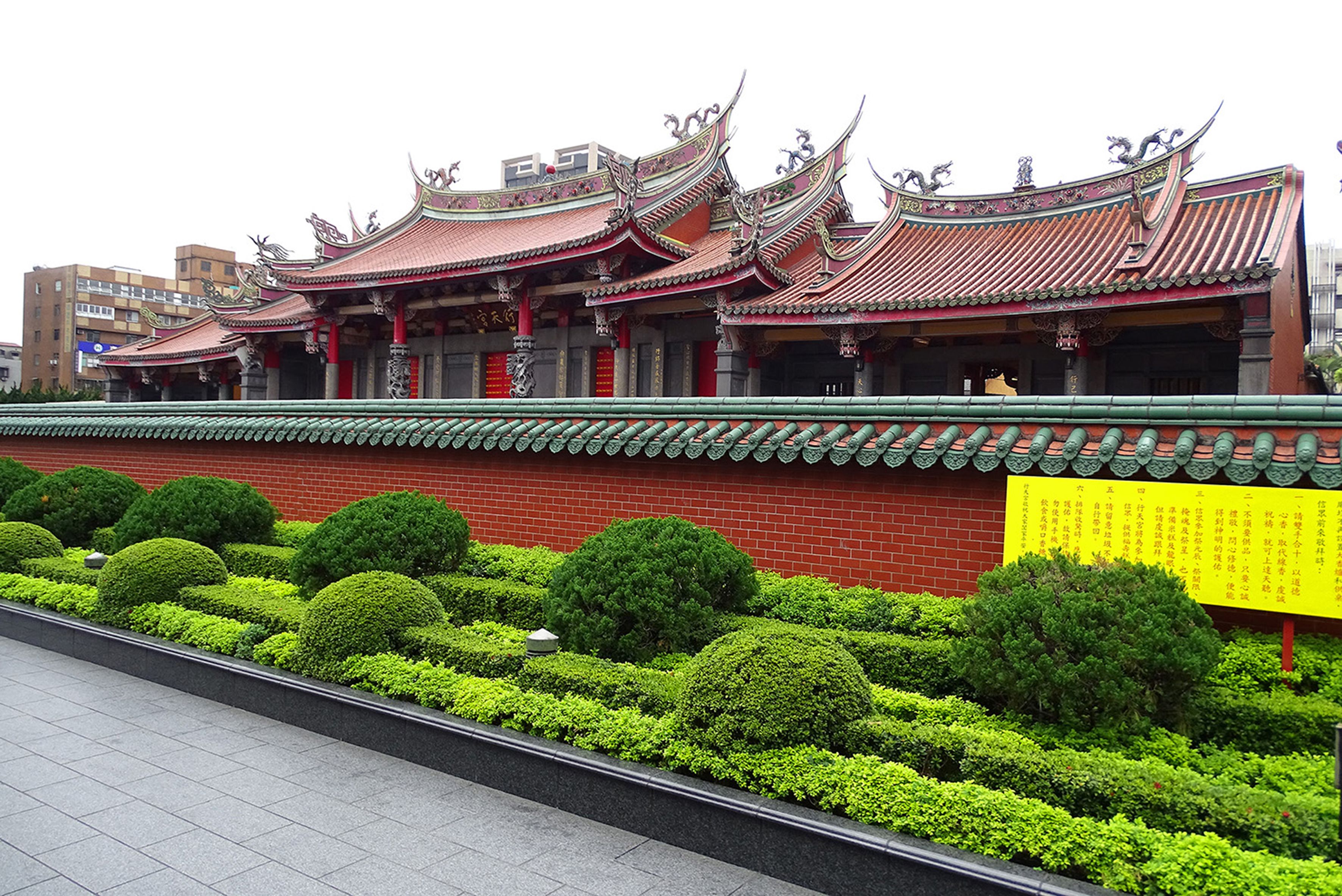 A traditional building with ornate roofs and a well-maintained garden with neatly trimmed bushes.