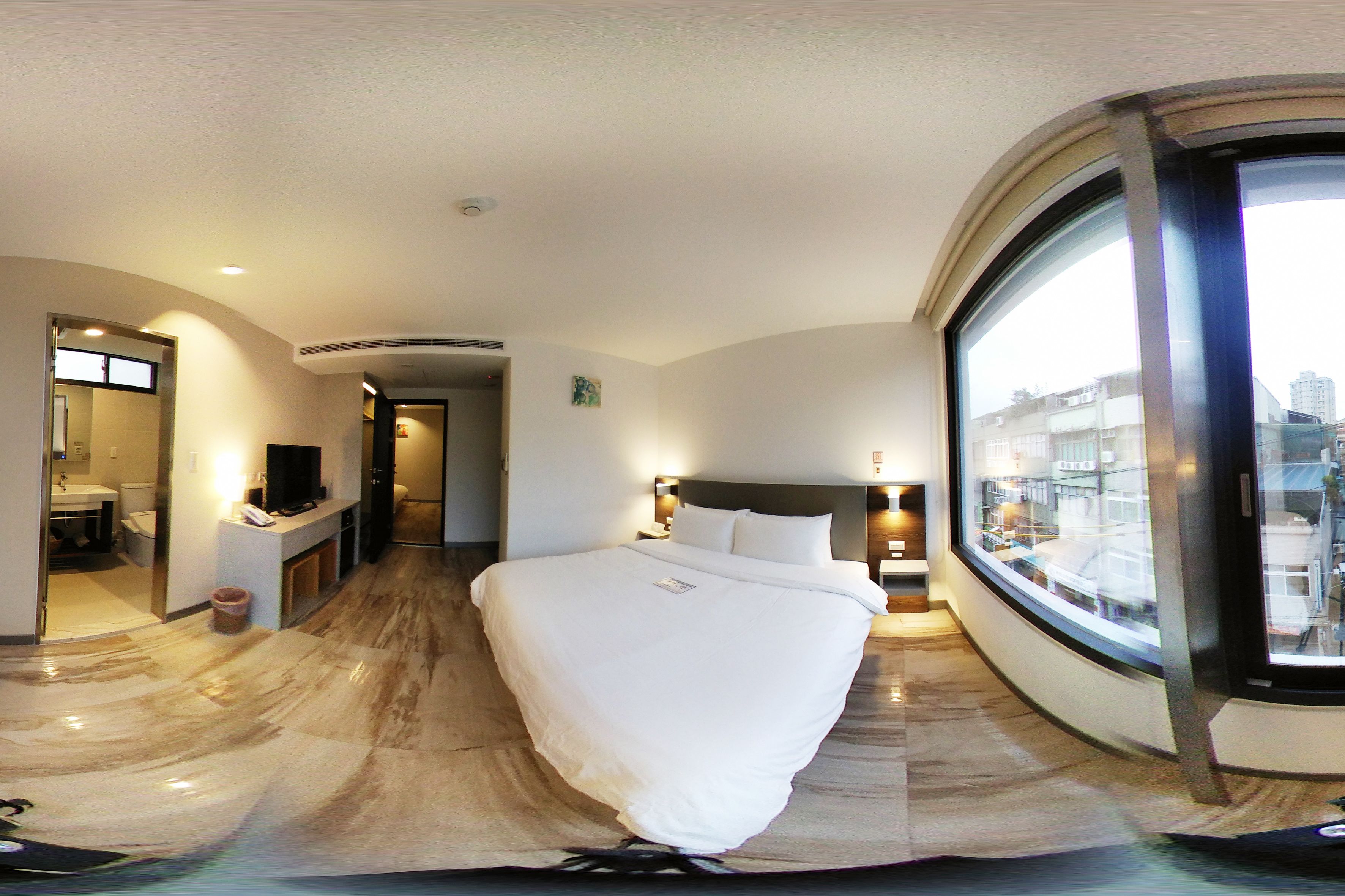 Een moderne hotelkamer met een groot bed, een badkamer en uitzicht op de stad door een groot raam.