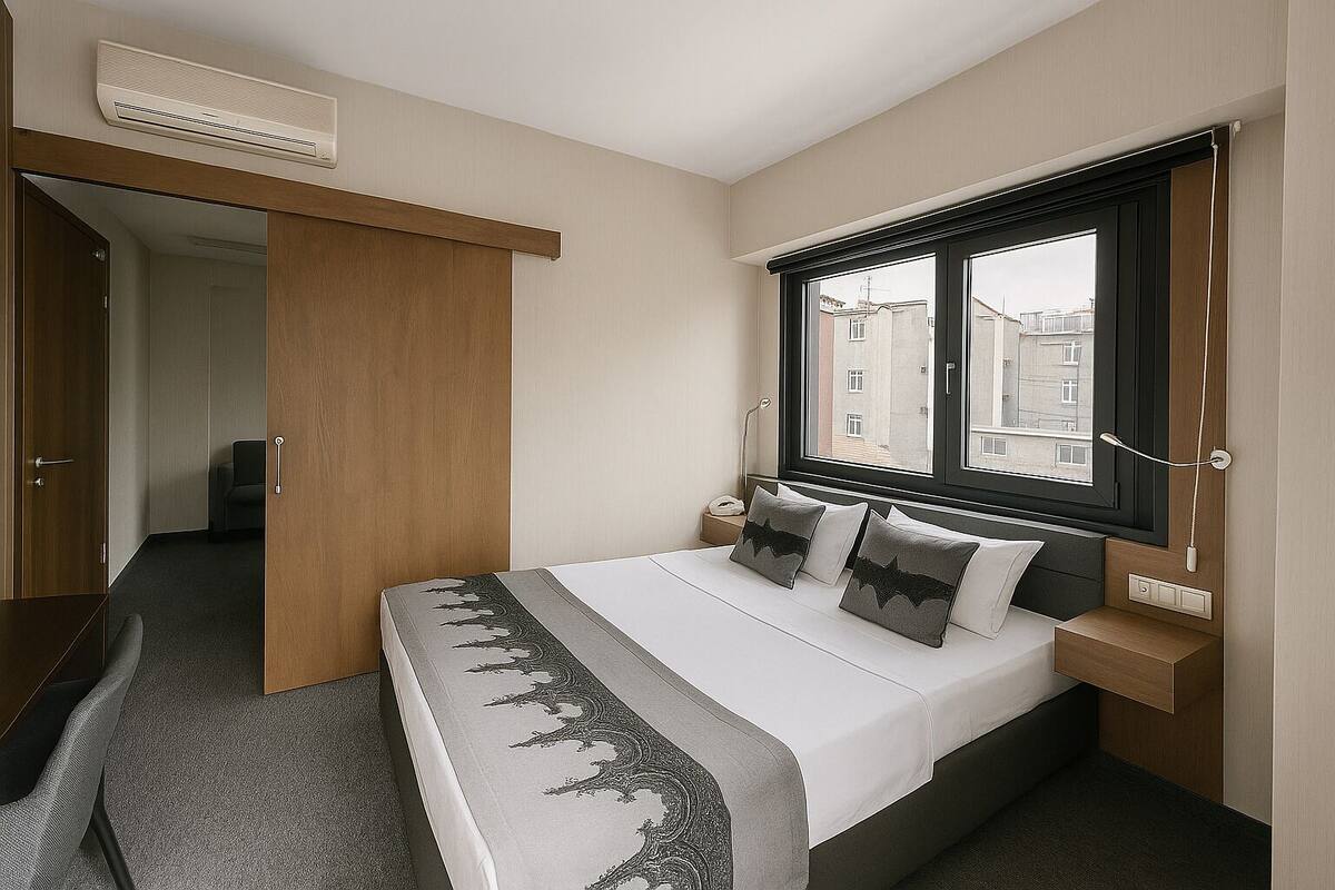 A hotel room with a bed, a window with a view, a bedside table, and a wardrobe.