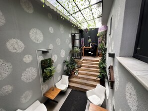 A modern interior with a grey patterned wall, a wooden staircase, white chairs, and potted plants. - Black Art Otel (Istanbul)
