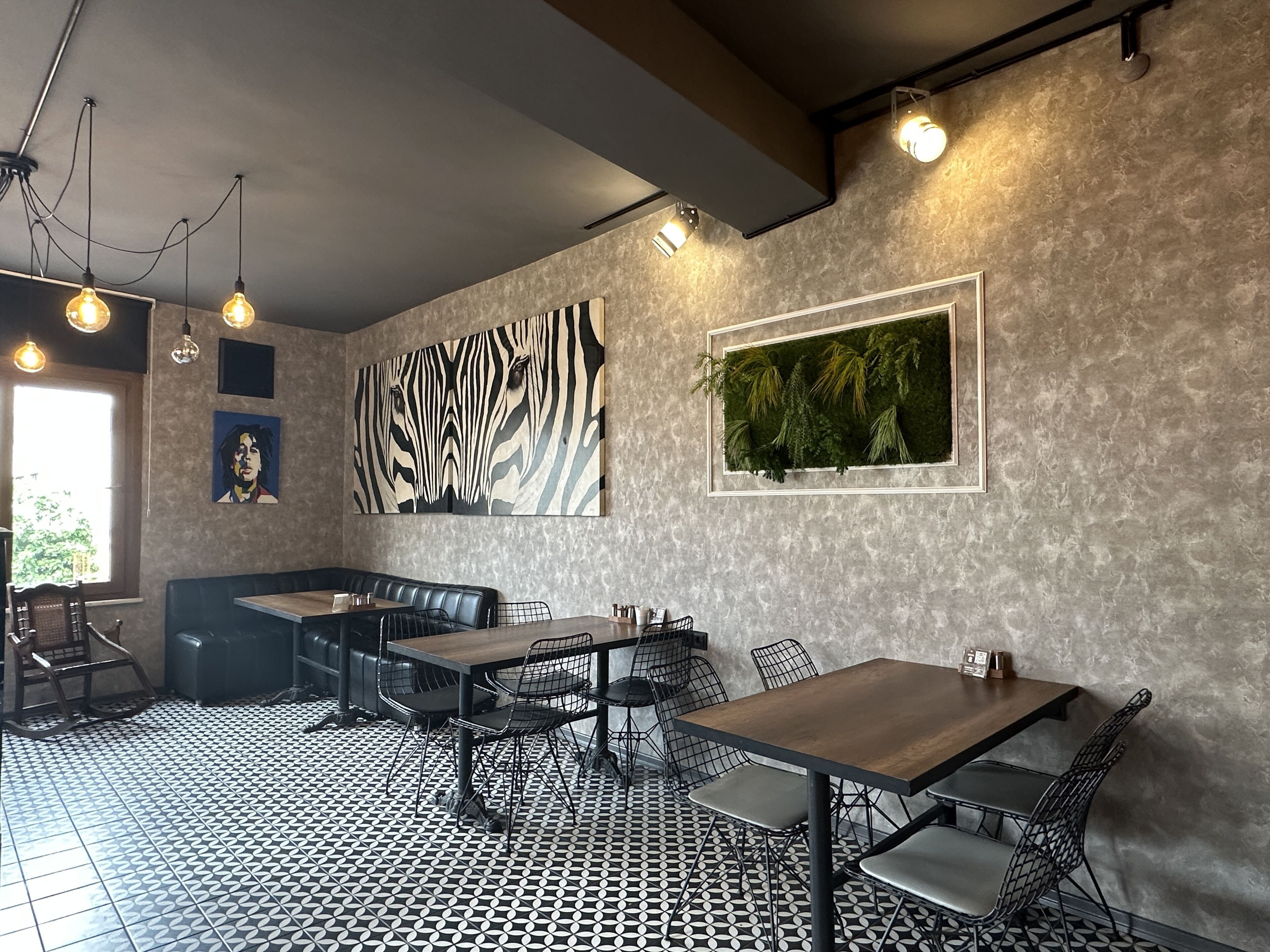 A restaurant interior with a patterned floor, a zebra mural, and a green plant wall.