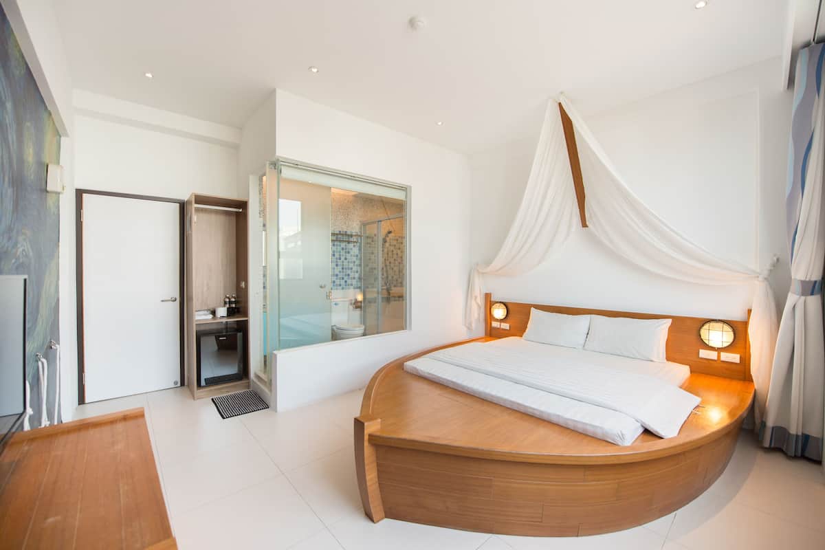 Un dormitorio moderno con una cama de madera curvada, cabina de ducha de vidrio y vestidor.