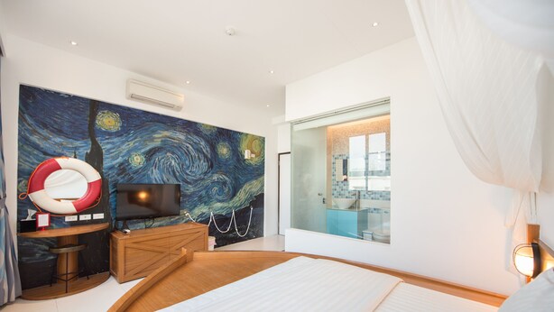A modern hotel room with a large bed, a television, a painting of a swirling night sky, and a view of the city through a large window. - Herman Hostel (Liuqiu)