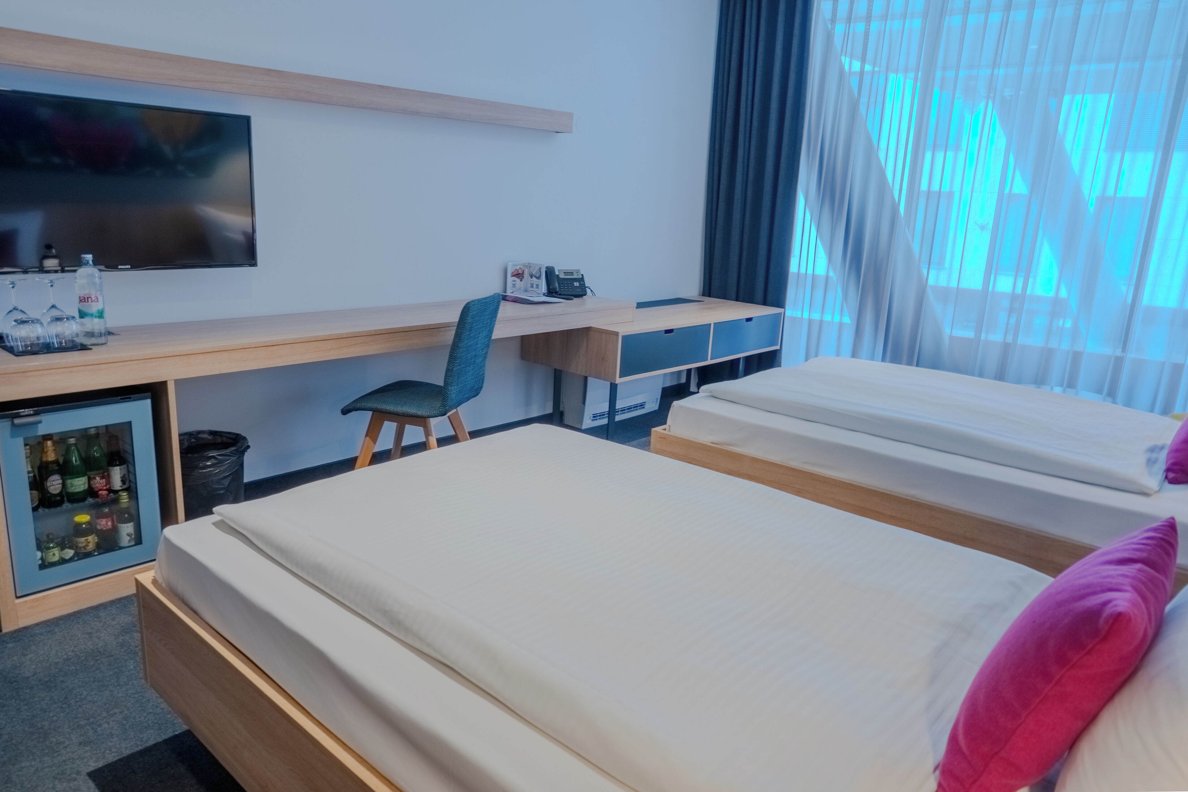 A hotel room with two beds, a desk with a chair, a television, and a minibar.
