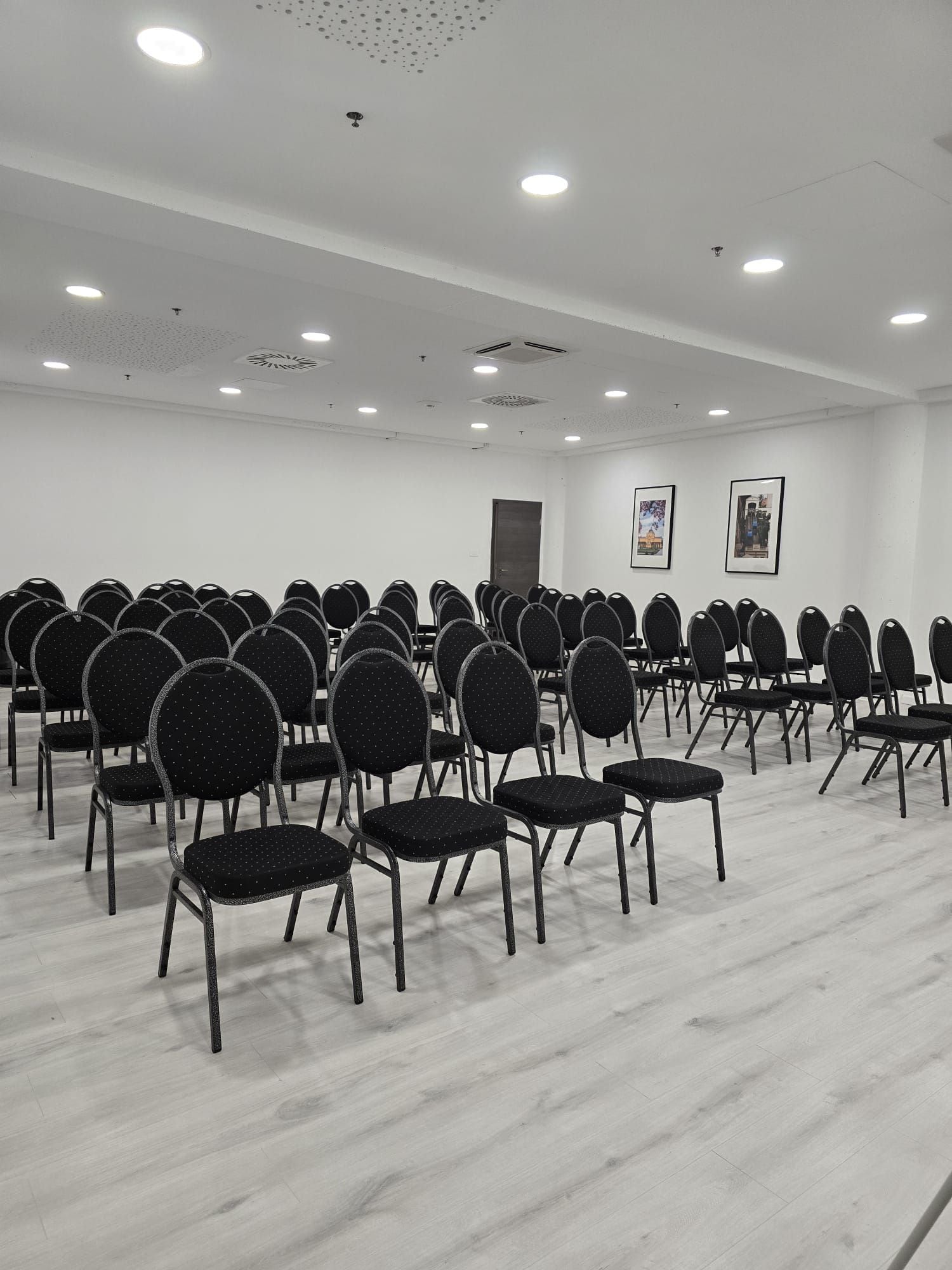 A conference room with rows of chairs, ceiling lights, and two framed pictures on the wall.