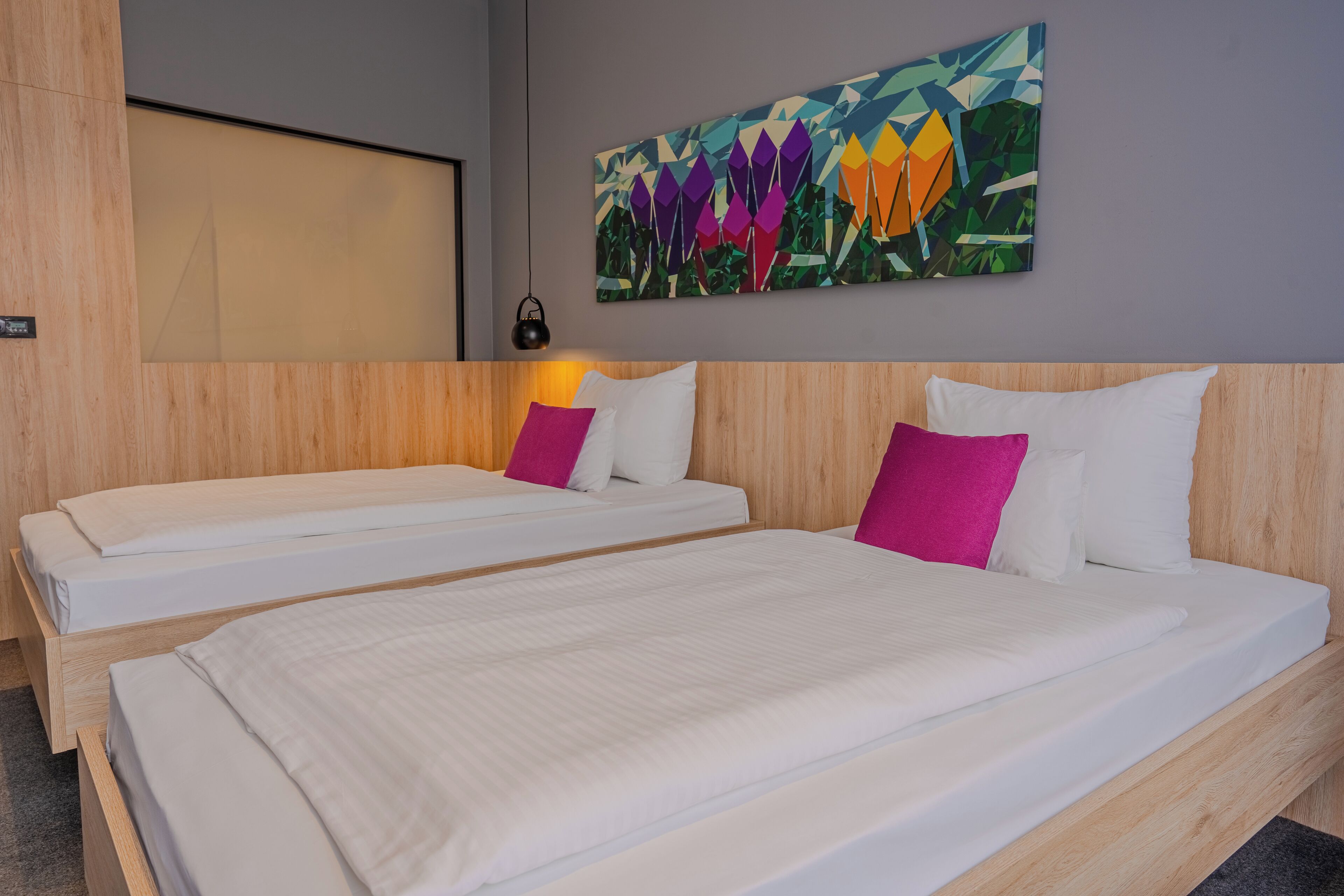 Habitación de hotel con dos camas individuales, cabeceros de madera y un cuadro abstracto colorido en la pared.
