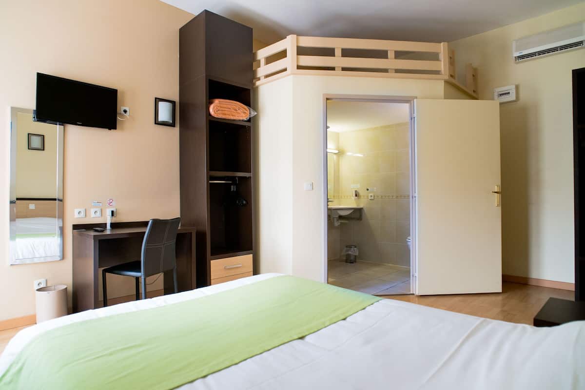 A hotel room with a bed, a desk, a chair, a TV, a wardrobe, and a bathroom.