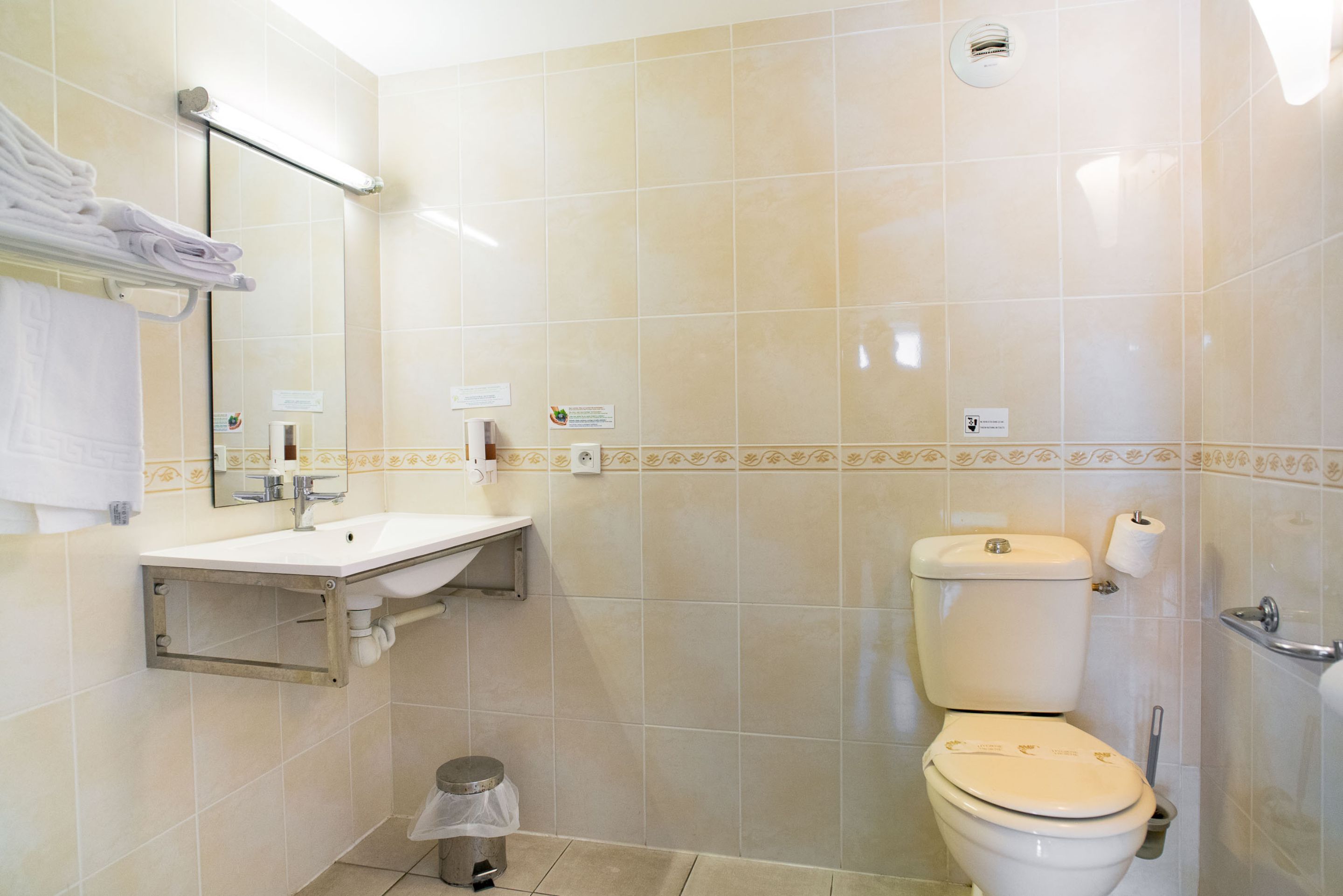 Baño con lavamanos, espejo, inodoro y un cubo de basura.