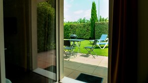 A glass door leading to an outdoor patio with a lawn, a barbecue grill, and two lounge chairs. - Allotel (Fos-sur-Mer)