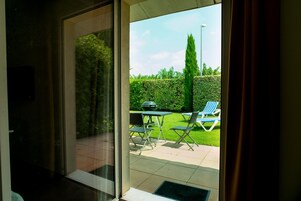 Puerta de vidrio que da a un patio exterior con césped, una parrilla y dos sillones de descanso.