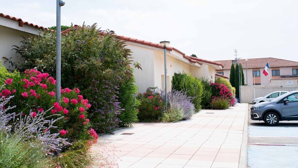 A residential street with a sidewalk, a parked car, and a building with a red-tiled roof. - Allotel (Fos-sur-Mer)