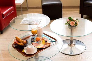 Bandeja de desayuno con cruasanes, huevos y bebidas sobre una mesa de cristal.