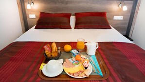 A neatly made bed with red and brown pillows, a breakfast tray with bread, fruit, eggs, and a jug of orange juice. - Allotel (Fos-sur-Mer)