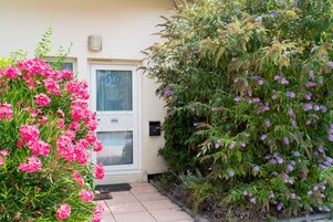 Una casa con una puerta que indica '806', rodeada de abundante follaje y plantas con flores.