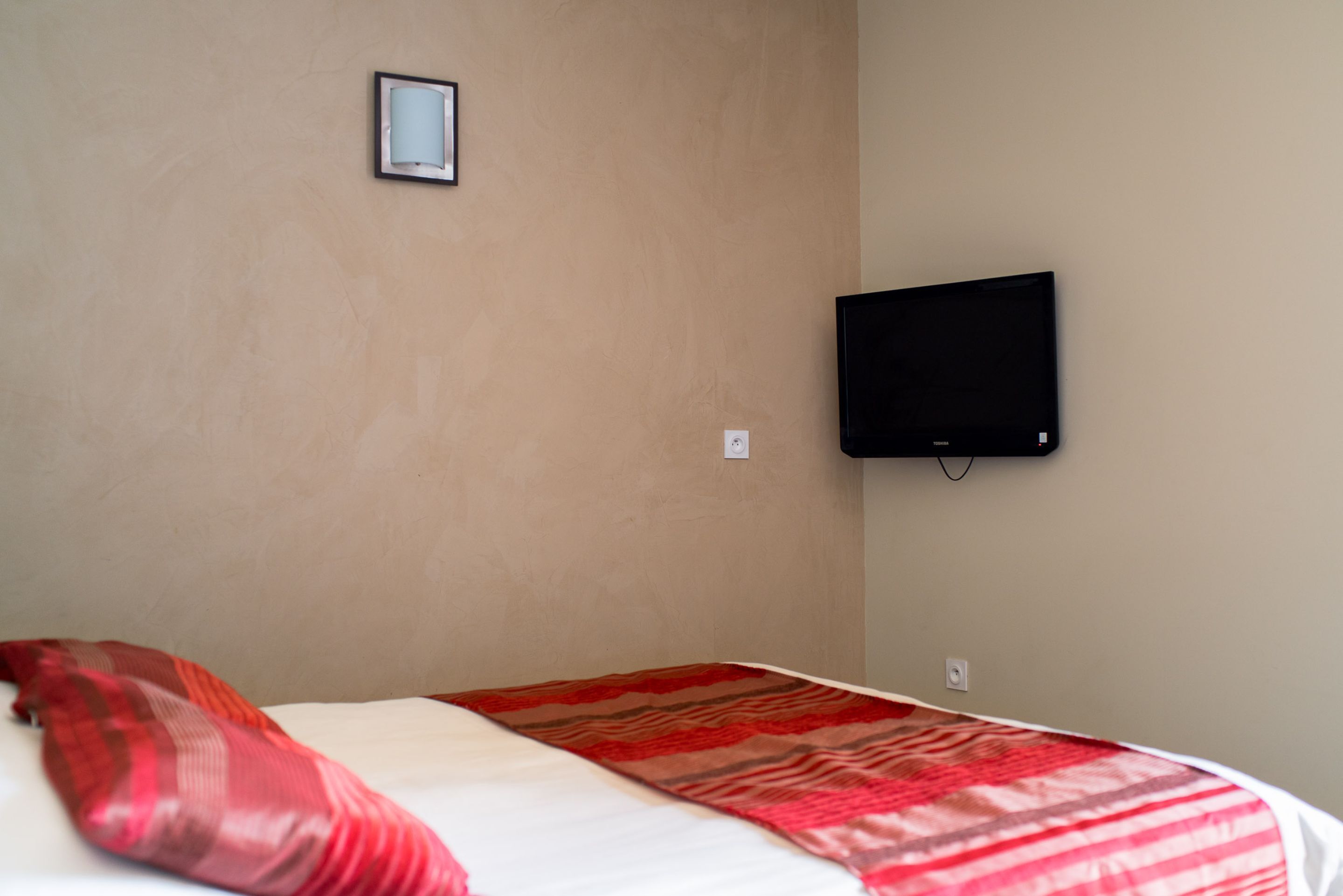 Habitación de hotel con una cama, un televisor en la pared y una pequeña foto en el marco.