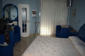 Habitació d'hotel amb un llit, dos seients blaus, escriptori amb cadira, mirall, finestra amb cortines i aire condicionat fixat a la paret.