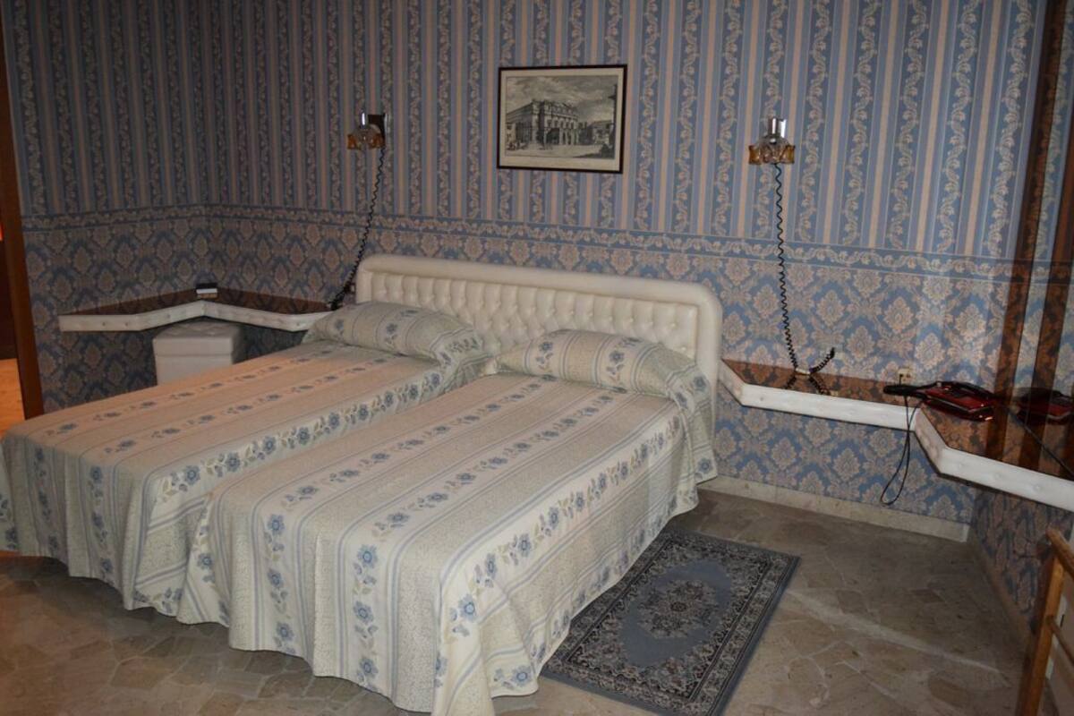 Une pièce comprenant un lit, un petit bureau et une chaise. Un des murs est décoré d’un motif et il y a un tapis sur le sol.