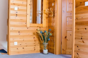 Un mur en bois orné d’un miroir, d’un porte-manteau et d’un vase contenant des fleurs séchées.