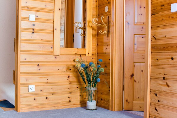 Eine Holzwand mit einem Spiegel, einem Kleiderhaken und einer Vase mit Trockenblumen.