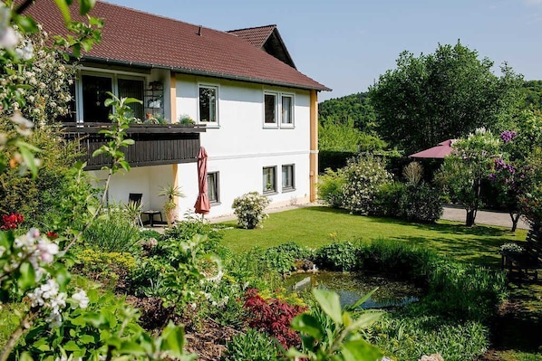 Ein zweistöckiges Haus mit Garten, Teich und einem Gebäude mit rotem Dach.