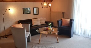 Uma sala de estar com sofá, duas poltronas, mesa de centro de vidro e luminária de chão.