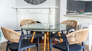 A round glass table with four chairs, a white fireplace, and a kitchen counter with utensils. - Vesperdene Mews 2 (Cape Town)