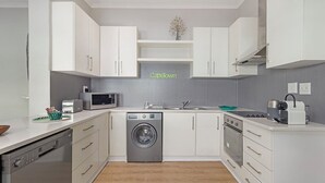 A modern kitchen with white cabinets, a washing machine, a microwave, and a toaster. - Vesperdene Mews 2 (Cape Town)