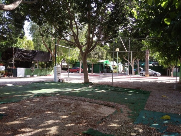 Un parque con área de juegos, árboles y una calle con coches estacionados.