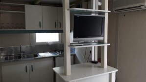 A kitchen with white cabinets, a built-in stove, a sink, and a flat-screen TV on a white stand. - Camping La Paz (Murcia)