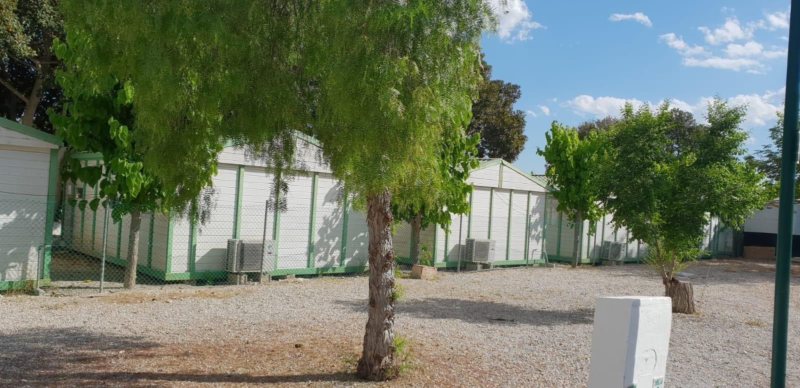 A row of white buildings with green trim, surrounded by gravel and trees.