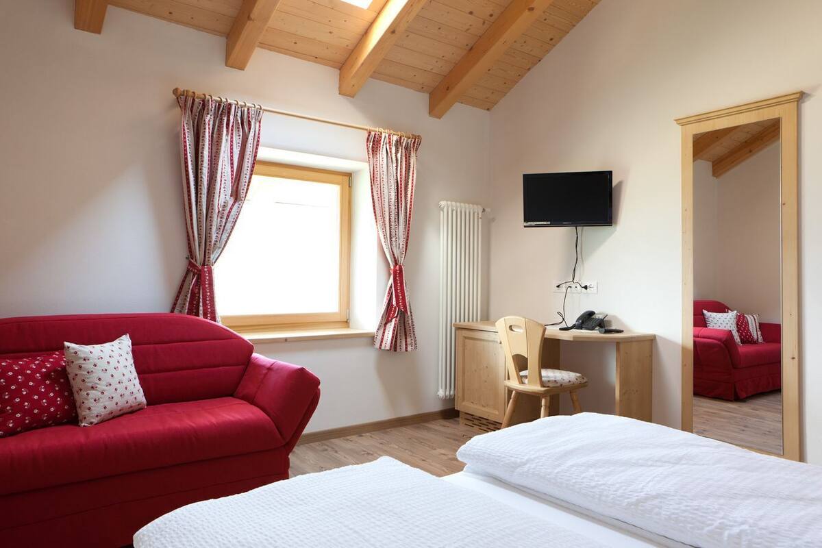 A room with a red sofa, a wooden desk, a television, and a bed.