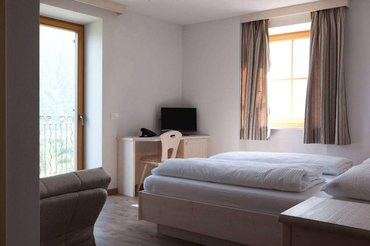A bedroom with a bed, a desk, a chair, a television, and a window with curtains.