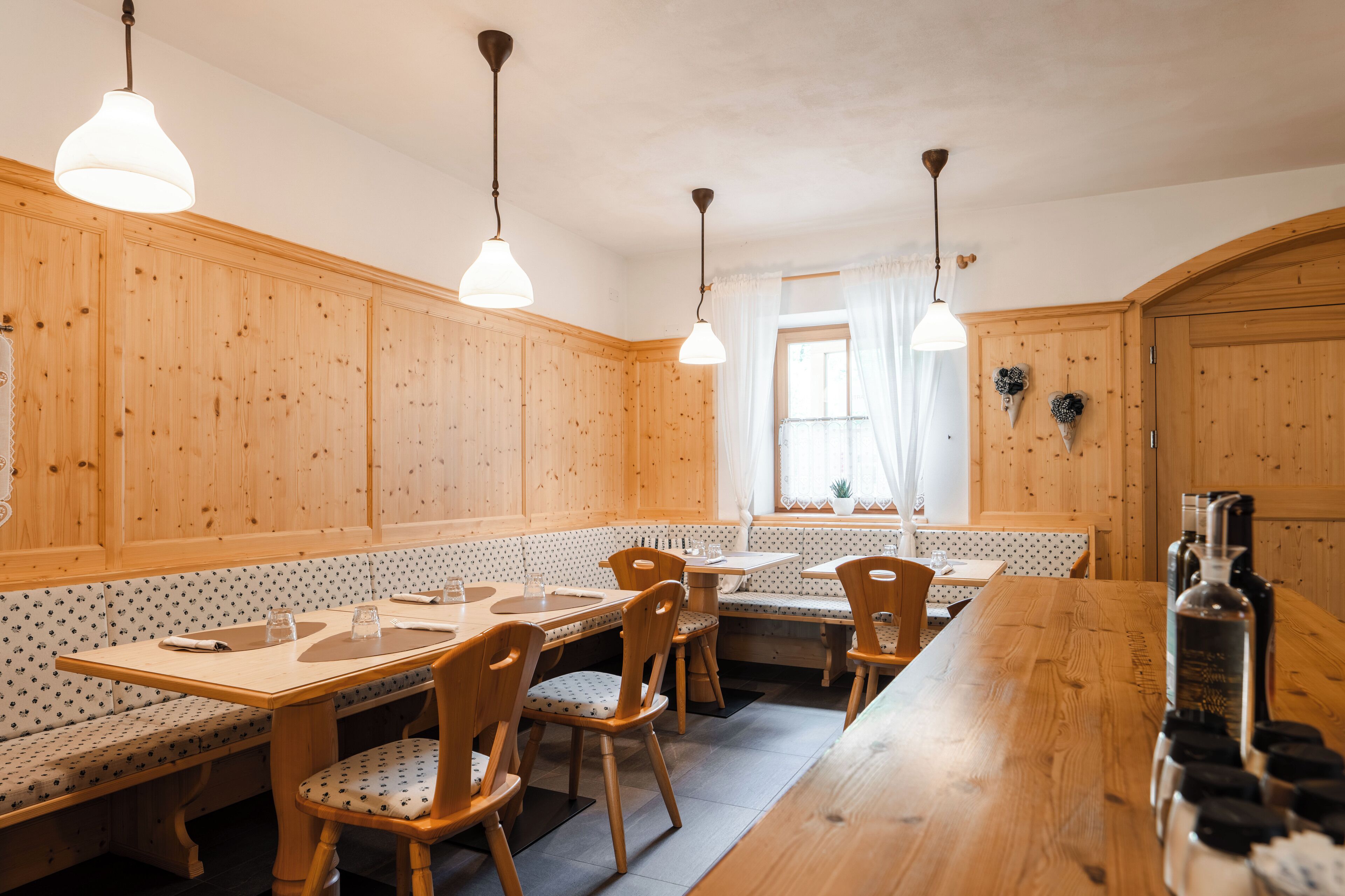 A wooden interior with a long dining table, benches, and hanging pendant lights.