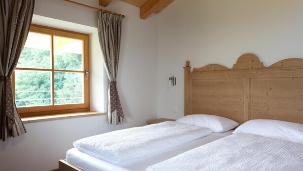 A bedroom with two beds, wooden headboard, and a window with curtains. - Coronata Haus (Roncegno)