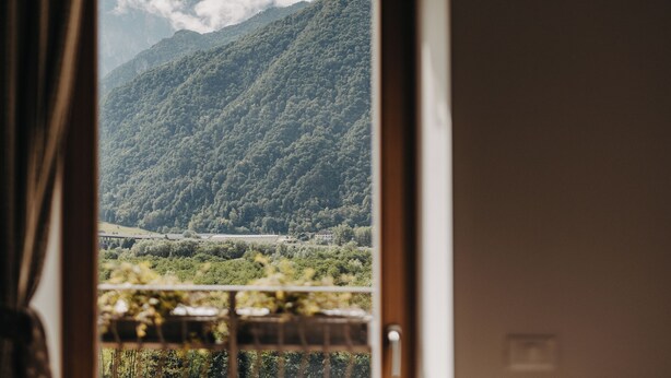 Une vue depuis une fenêtre à cadre en bois, donnant sur un paysage montagneux avec une végétation luxuriante et une vallée en contrebas.