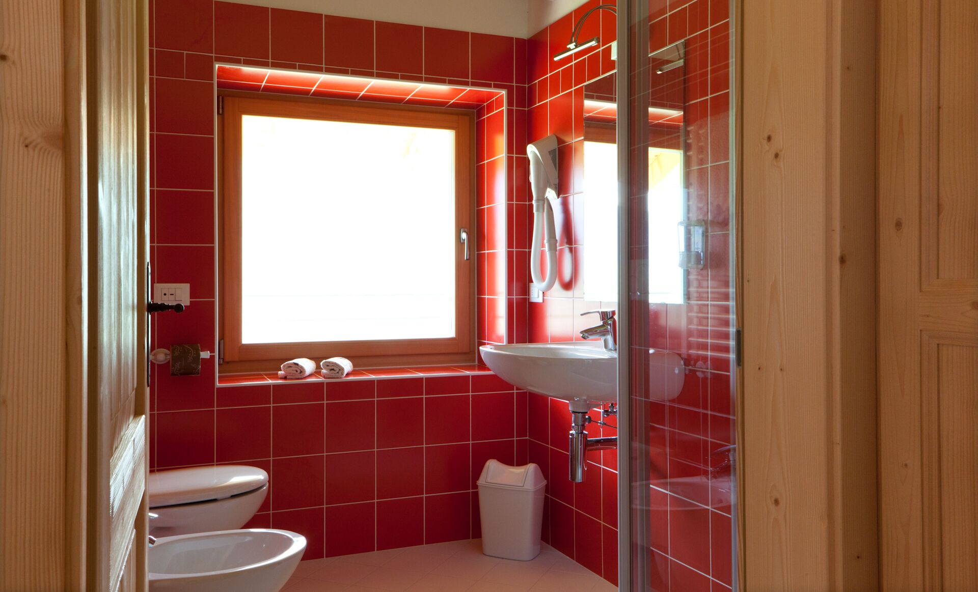 Un baño con baldosas rojas, una ventana, un lavabo e inodoro.