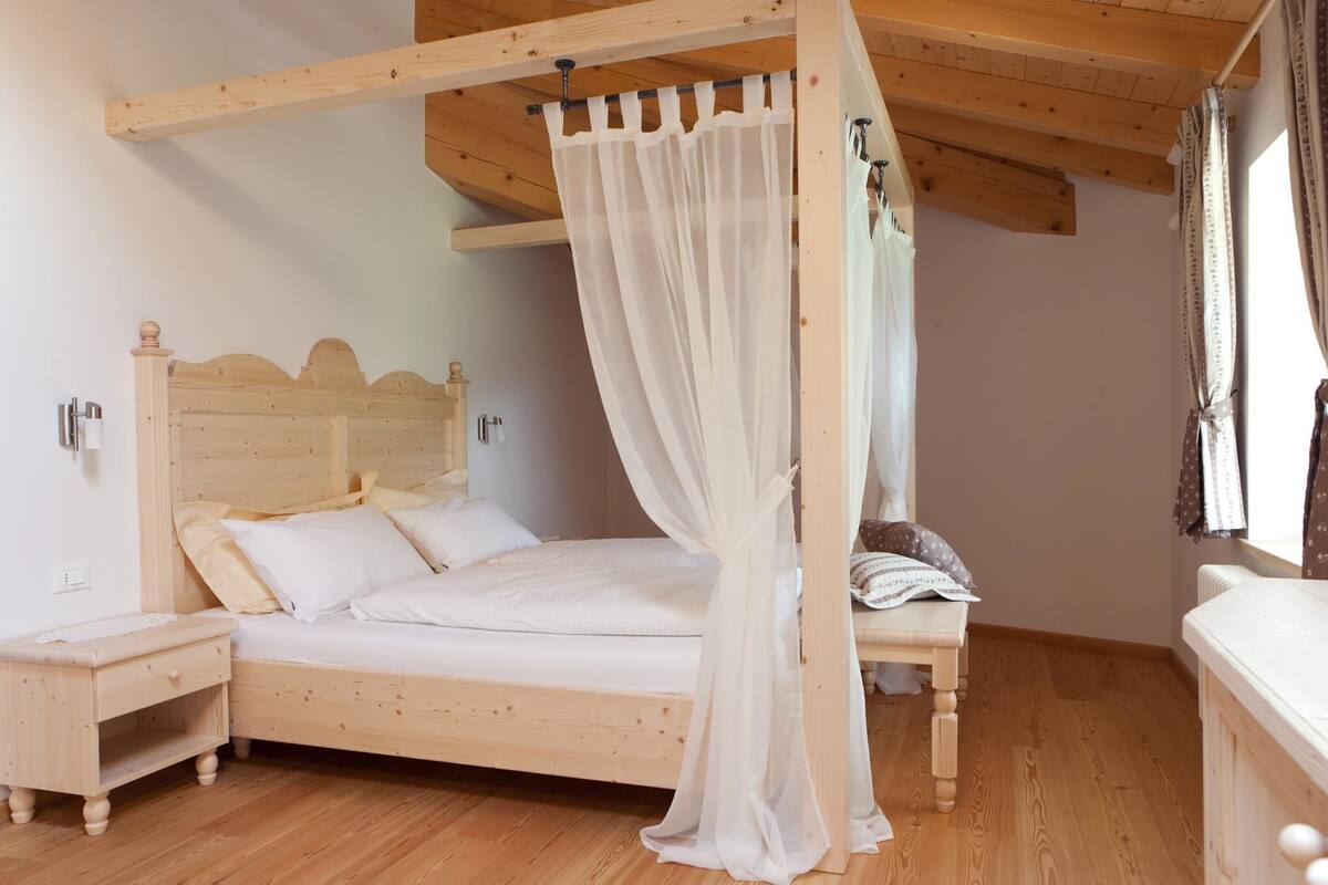 A wooden four-poster bed with a canopy, a nightstand, and a dresser in a room with wooden floors and walls.