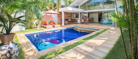 A modern house with a swimming pool, outdoor seating, and lush greenery.