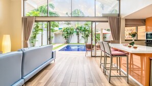 A spacious living area with a large window, a pool, and a kitchen area. - 2 Bedrooms Villa Aperol (Koh Samui)
