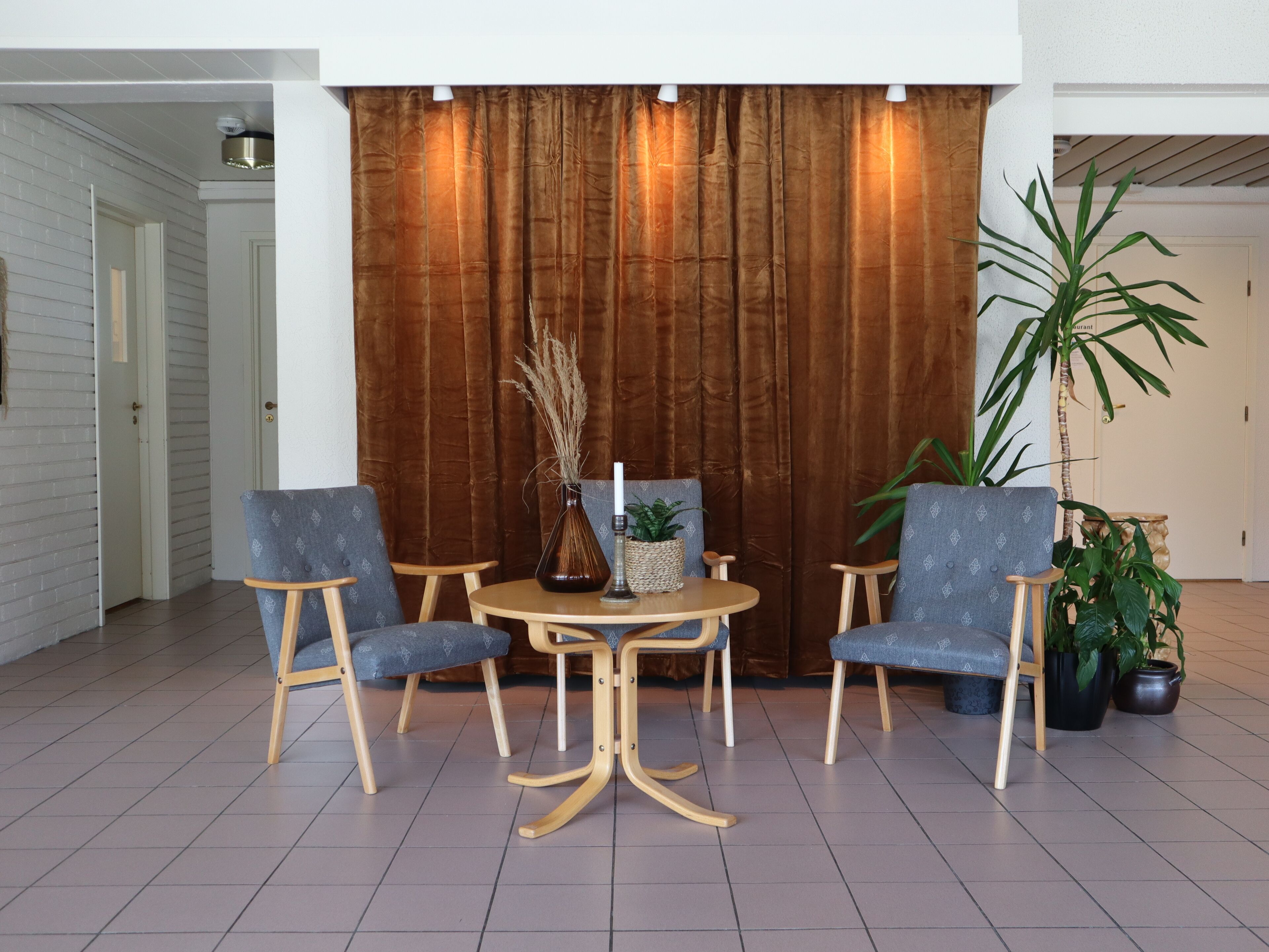 A room with a brown curtain backdrop, two blue upholstered chairs, a small round table, and a potted plant.