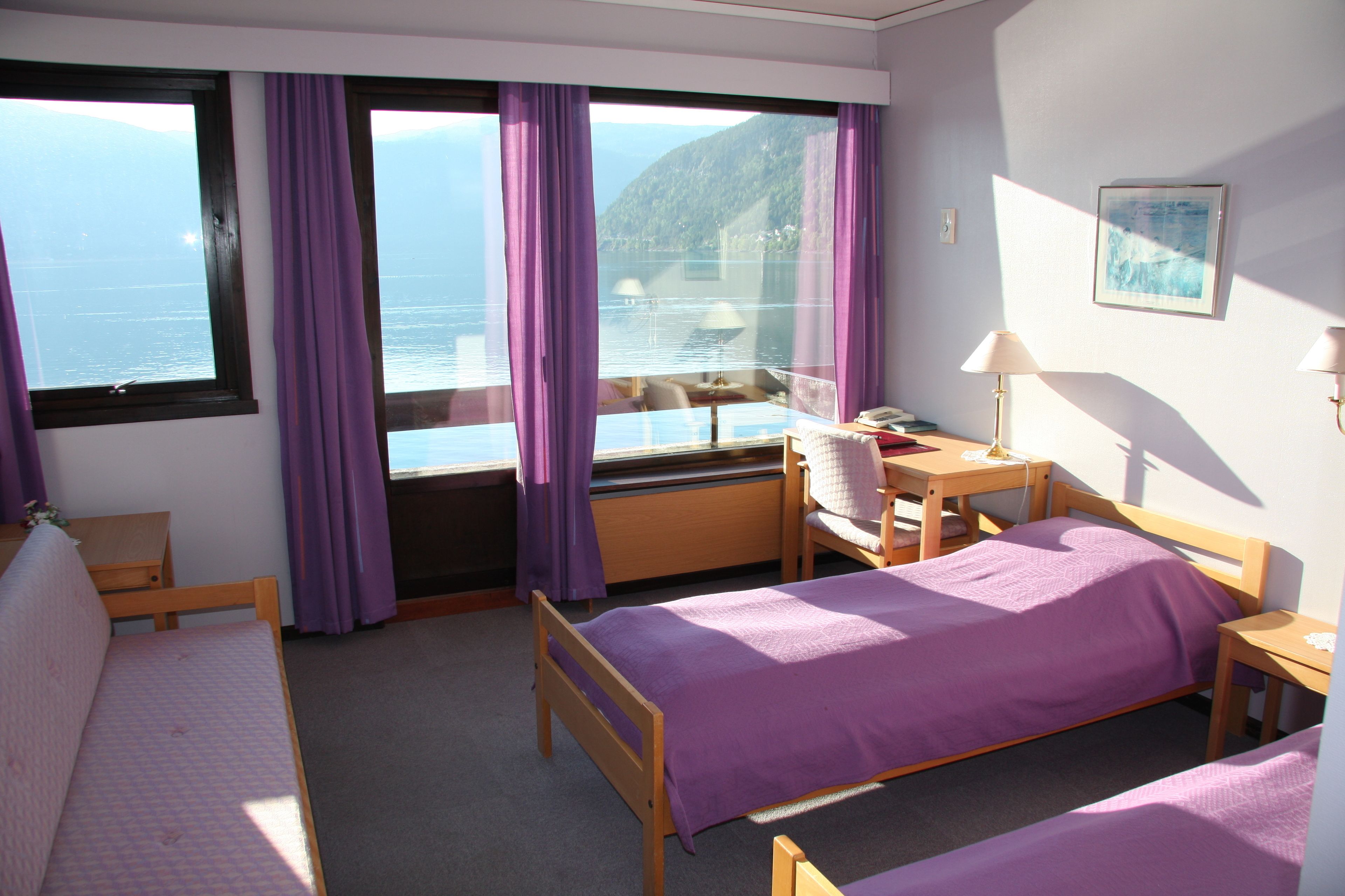 A room with two beds, a desk, a chair, and a view of the sea through large windows.