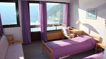 A room with two beds, a desk, a chair, and a view of the sea through large windows.