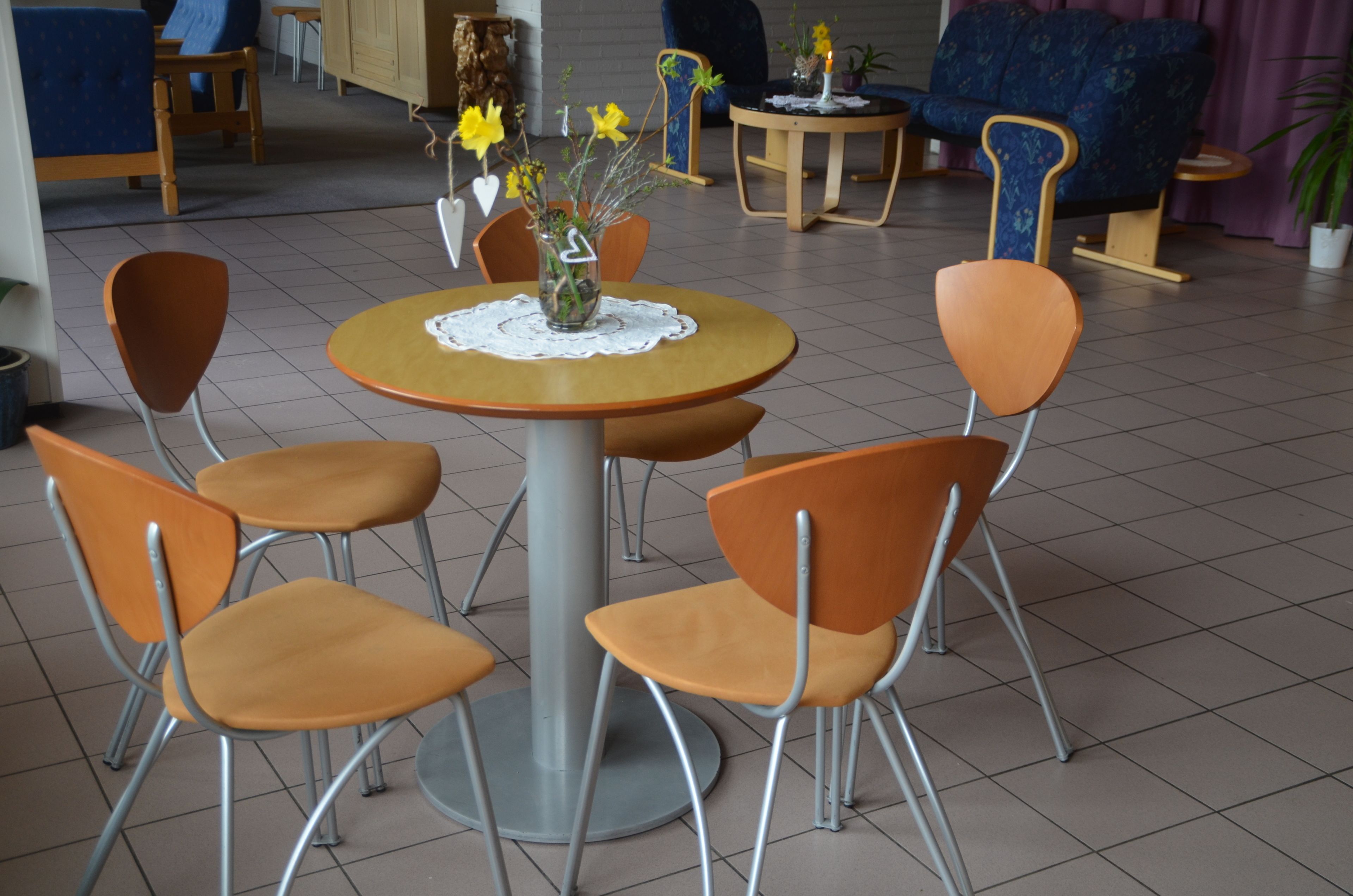 A round table with a vase of yellow flowers, surrounded by four orange chairs.