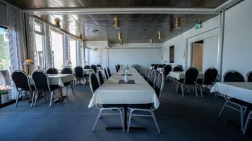 A conference room with multiple tables and chairs, large windows, and ceiling lights.